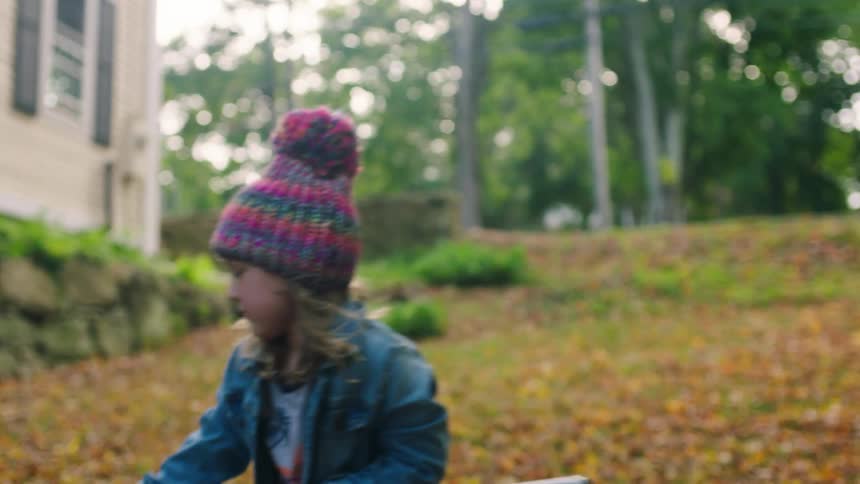 Little girl standing outside of a house with a rake raking leaves into a pile