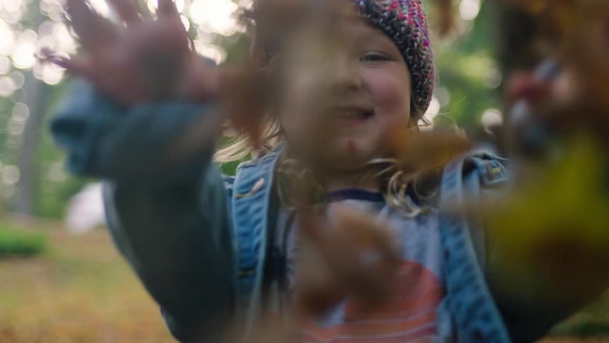 Little girl playing outside tossing bunches of leaves up into the air
