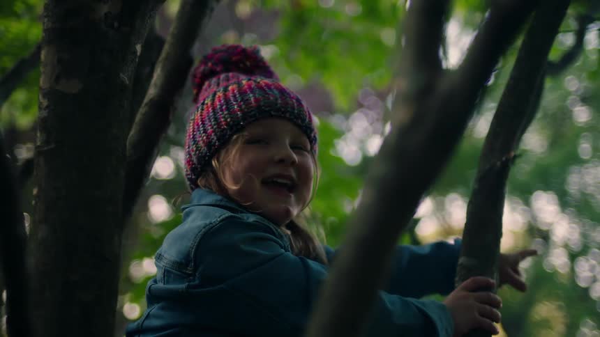 Little girl with a beanie and denim jacket stands on a tree and laughs