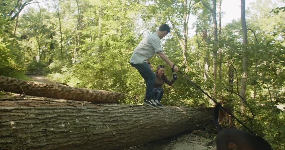 Man holding the hand of a woman helps her walk over a tree trunk in the forest