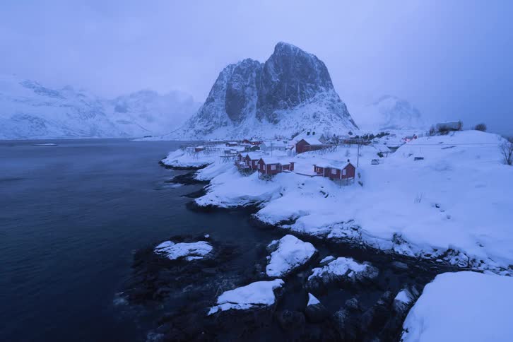 Small town in the arctic covered in snow beside ocean where people go in and out and lights come on and off