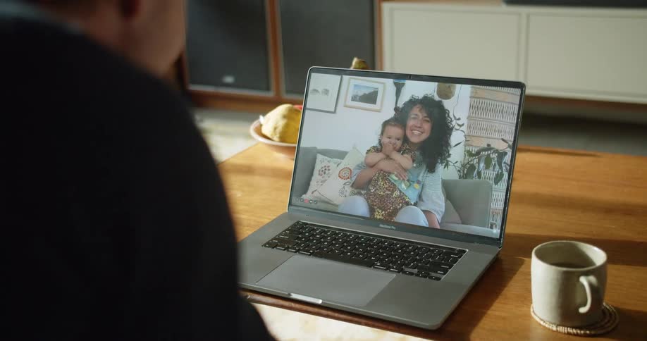 Man waves and blows kisses to a woman and a baby that he is talking with on his computer screen