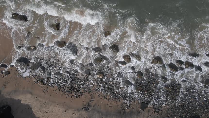 Aerial view of ocean waves crashing against rocky shore