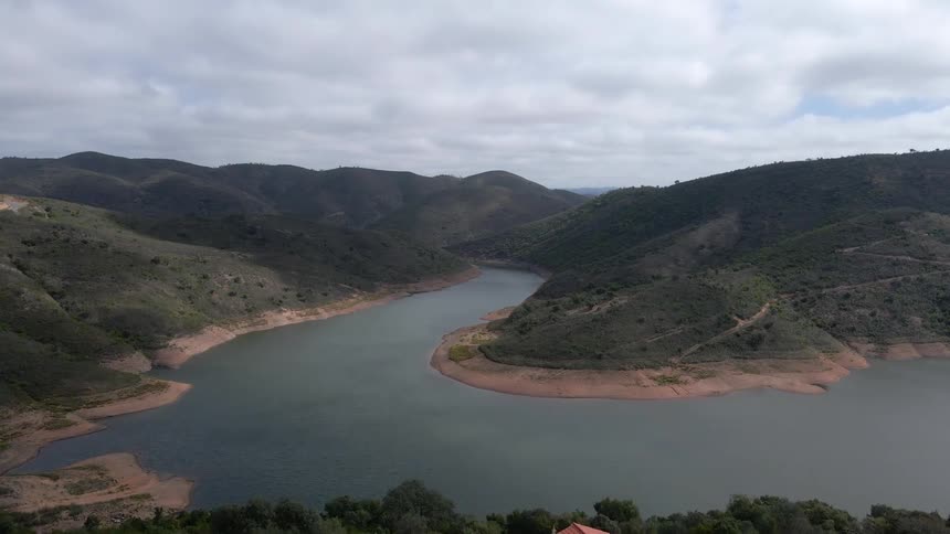 An aerial view of houses on a hillside overlooking water with hills all around during the daytime