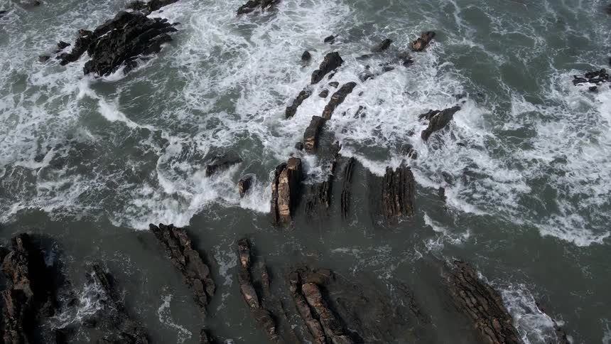 Aerial view of foamy ocean waves crashing against the rocky shore