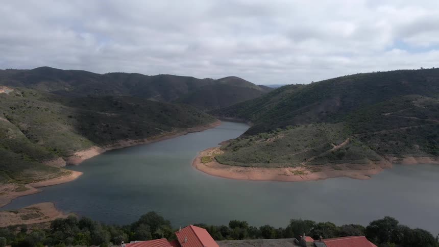 Wide aerial shot of a river with green hills that opens up to homes set atop of a hill