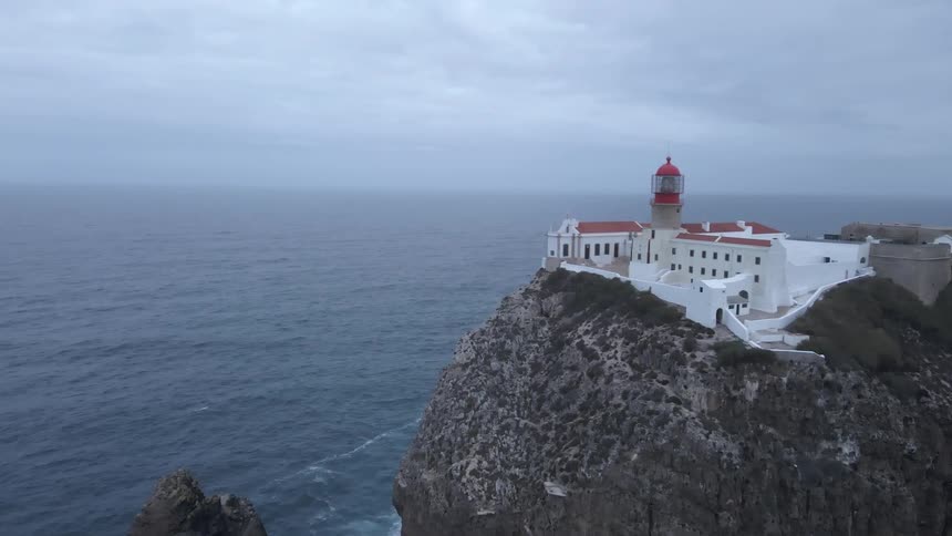 A large resort with white walls and a domed tower sits on the edge of a cliff overlooking the ocean