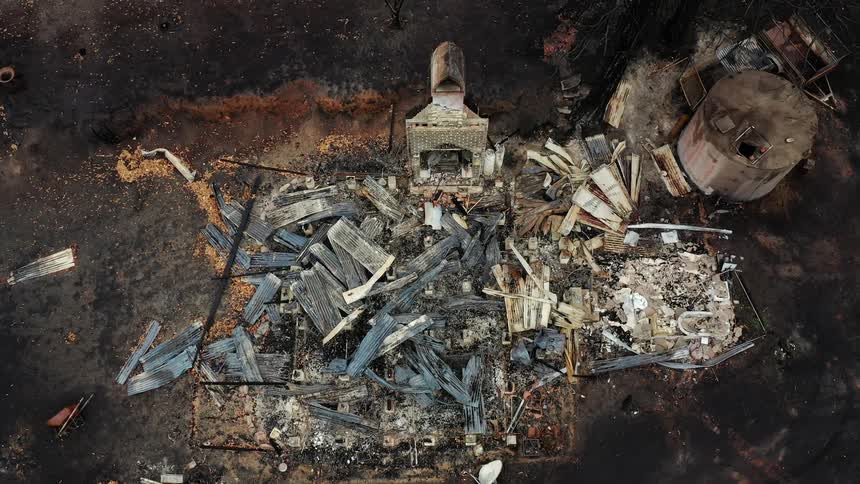 Wrecked truck sits next to burned damaged factory building and tanks