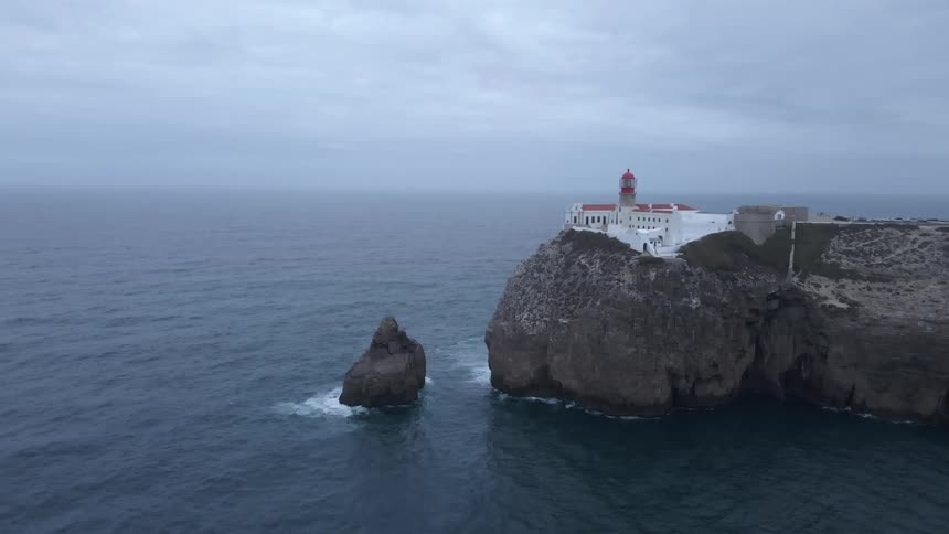 Lighthouse building on cliff overlooking ocean on a cloudy day
