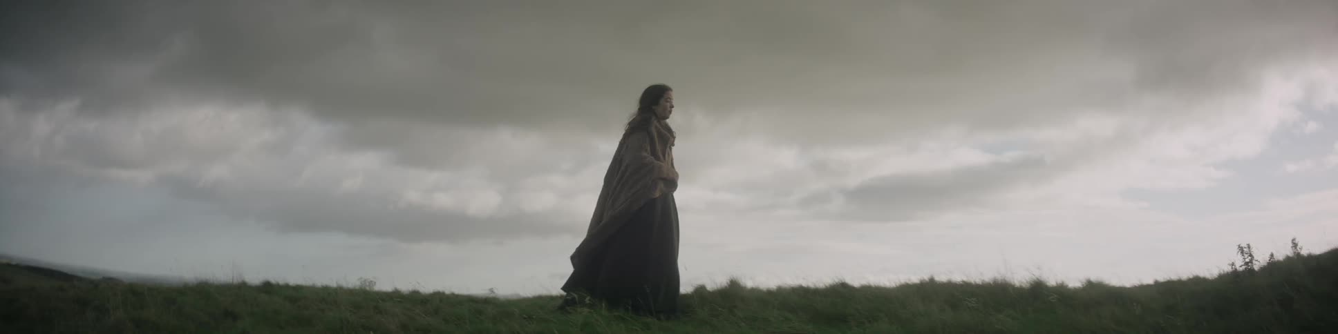 A woman is standing on a grass field on a cloudy day
