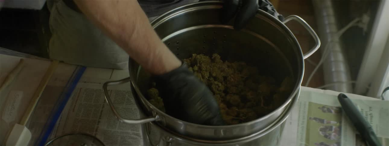 Man stands and mixes plant material in large metal pot