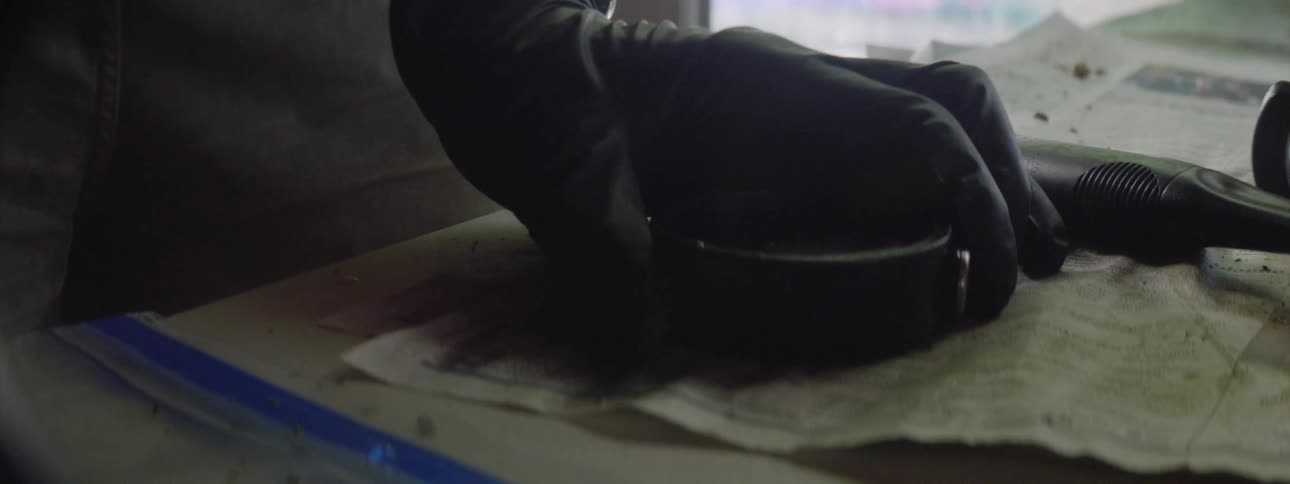 A man working on repairs picks up a vehicle gas cap off a table covered with newspaper