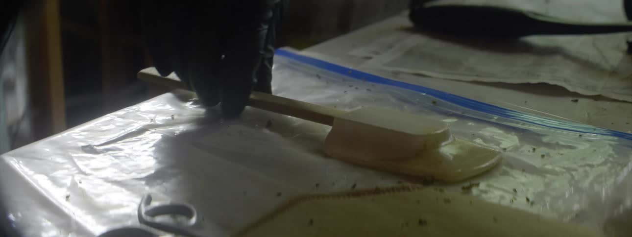 A hand picks up a white spatula from a table with a plastic bag newspaper and scissors next to it