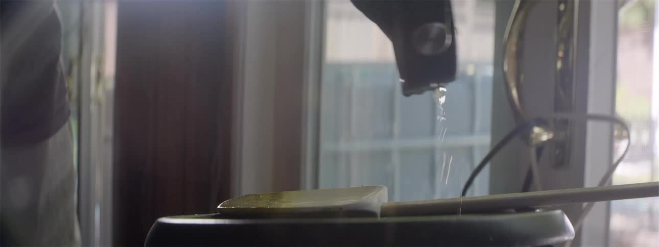A person dumping water from a small bowl into a planter