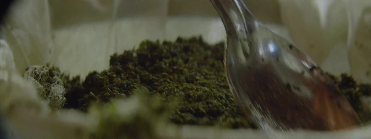 A spoon is placing green food into a white bowl with cheesecloth