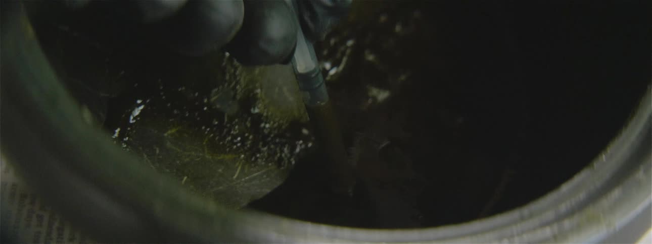Person wearing black gloves draws liquid into syringe from mixture in pot sitting on newspaper