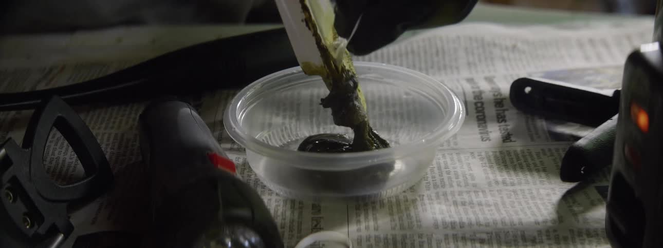 Worker scraping a paste off of a spatula putting it into a small clear container