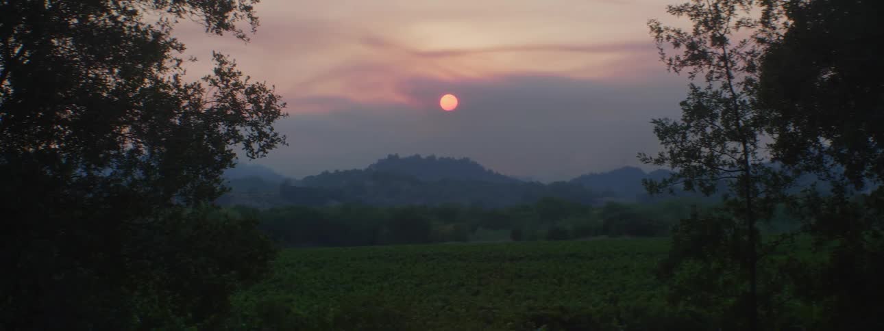 A full red moon looms over a countryside of mountain and forest in the evening