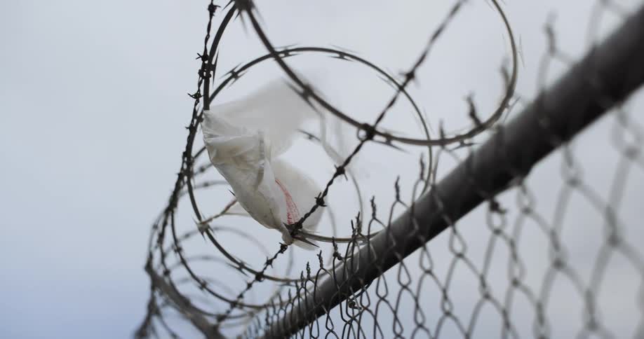 A white piece of fabric is stuck to a barbed wire on top of a fence