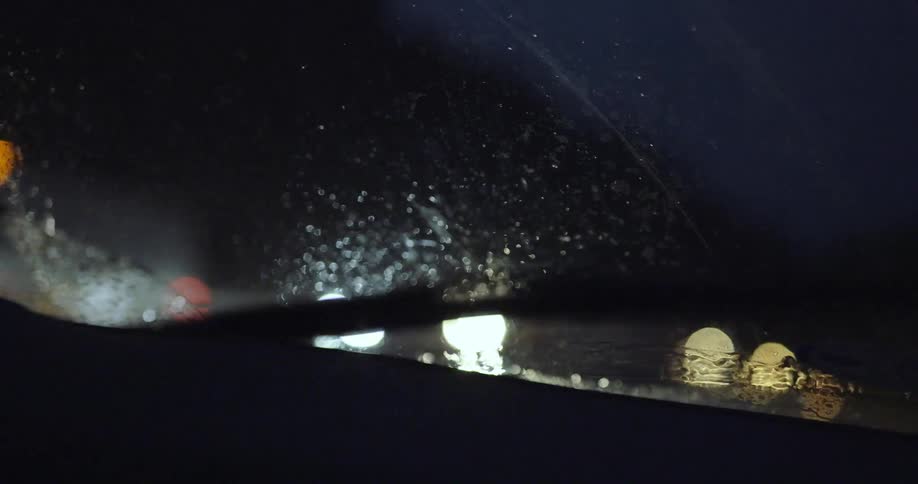 Interior of car driving down a street in the rain with the windshield wipers on