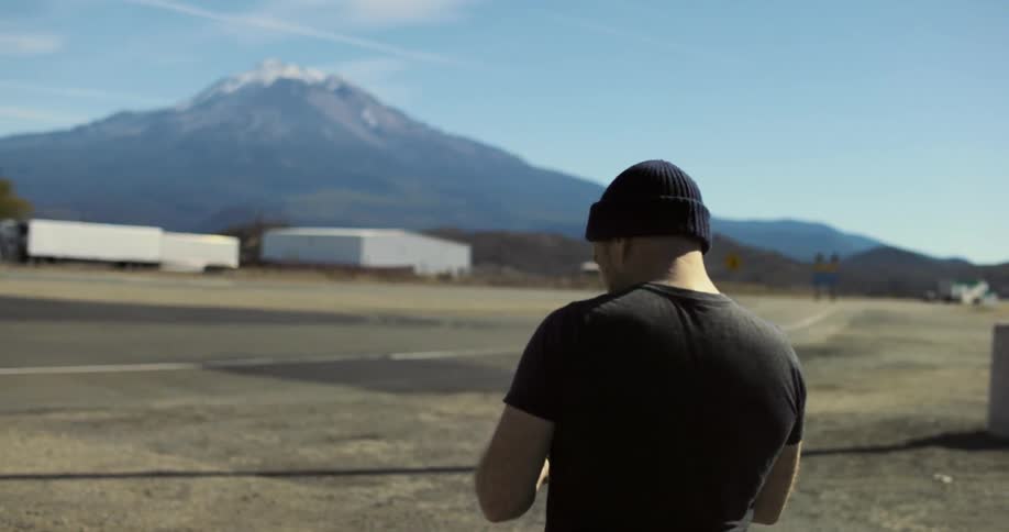 A man takes a photo with his phone at a rest stop of nearby mountains
