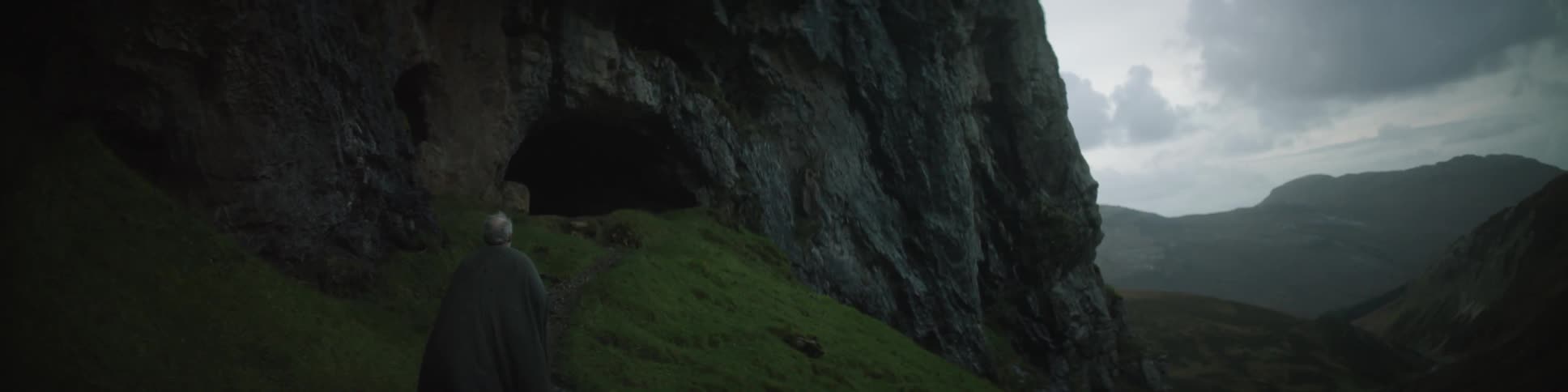 Man dressed in a cloak walking toward a cave