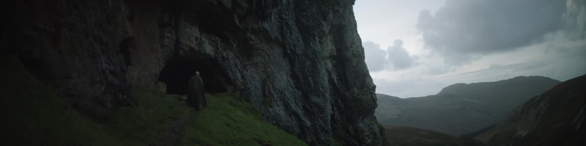 A man is standing outside a cave on a cloudy day