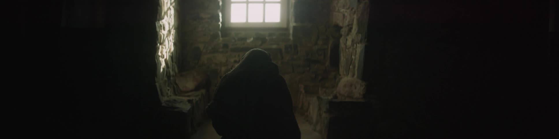 A dark figure is sitting in a room by a window