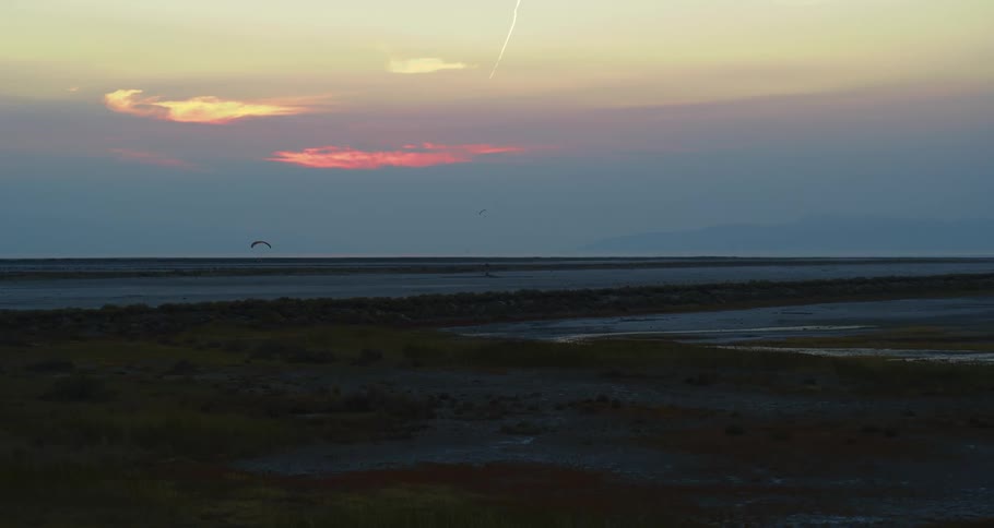 People parachuting across a wide grassland at sunset