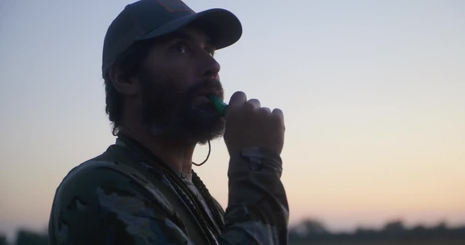 A man is hunting outdoors scanning the sky with a whistle in his mouth