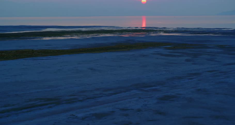 Aerial view of the ocean in a deep blue color with the sunset in the horizon