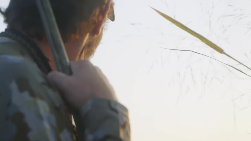 A hunter sits in a field with a rifle in his hand and a dog near him
