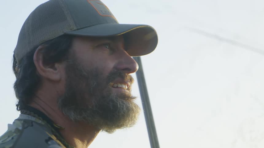 Man with beard wearing baseball cap scans area standing under blue sky