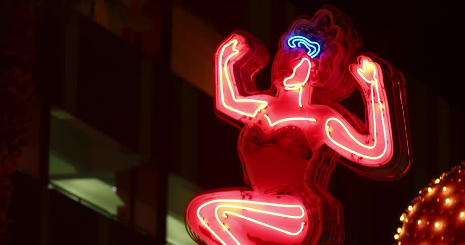 Neon sign in form of girl blinks with different colors near parking garage at night