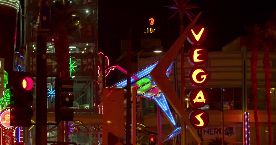 Large neon sign flashing vegas and an arrow in a downtown area
