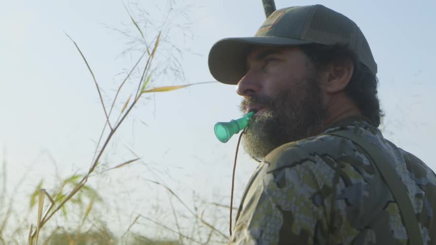 A male hunter stands outside with a whistle in his mouth