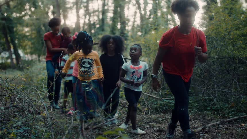 Woman leads group of people most of them children along trail through woods