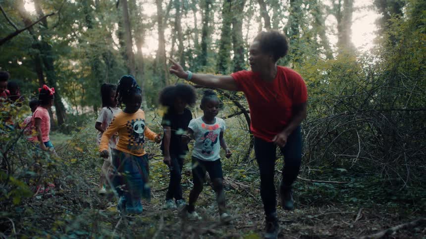 A woman is pointing out things in the forest to her students