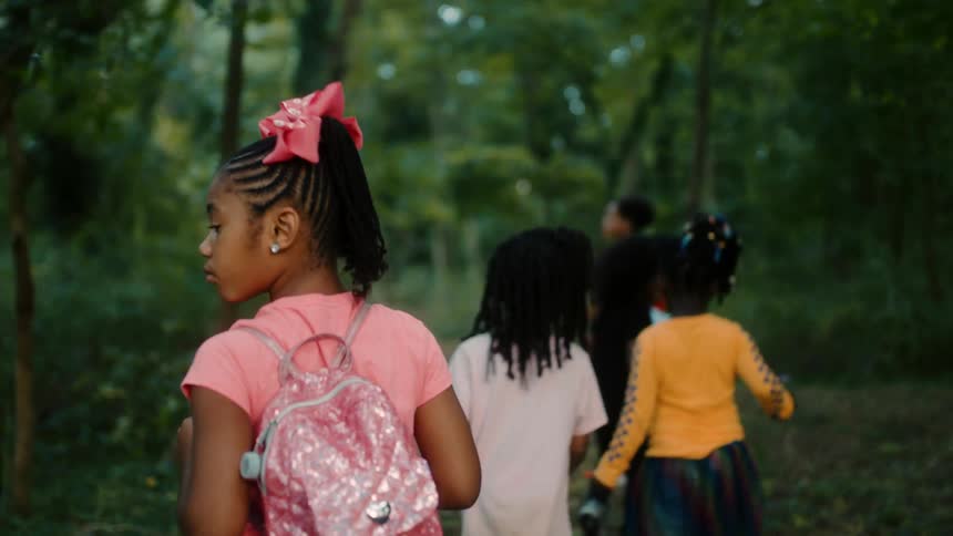A group of young kids walk through the woods in a single file line