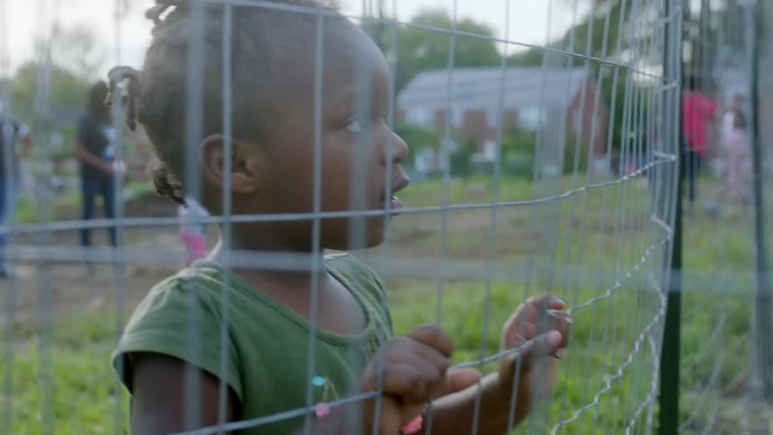 A little girl standing while holding on to a fence outdoors