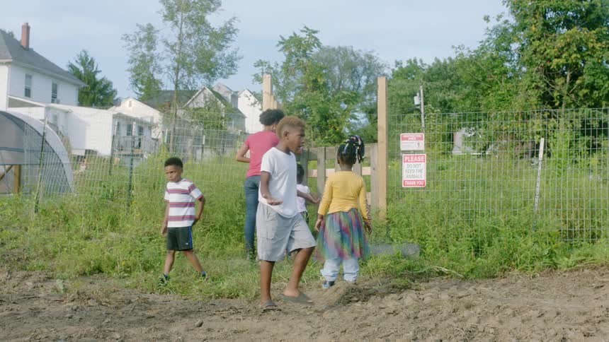 A mother in a village opens a gate so her children can go in a pen and see an animal