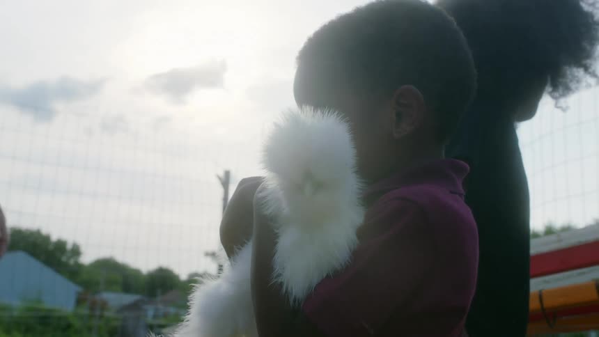 A boy smiles as a woman helps him hold a white chicken on farm
