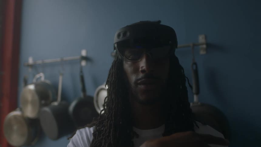 Man standing in a kitchen wearing a goggle headset pointing his finger around in the air