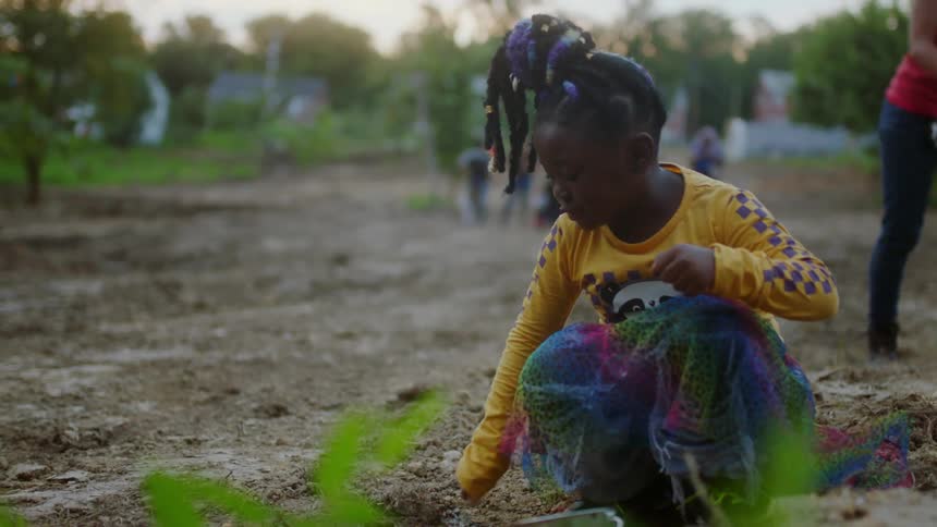 Girl crouches near the ground playing in the dirt