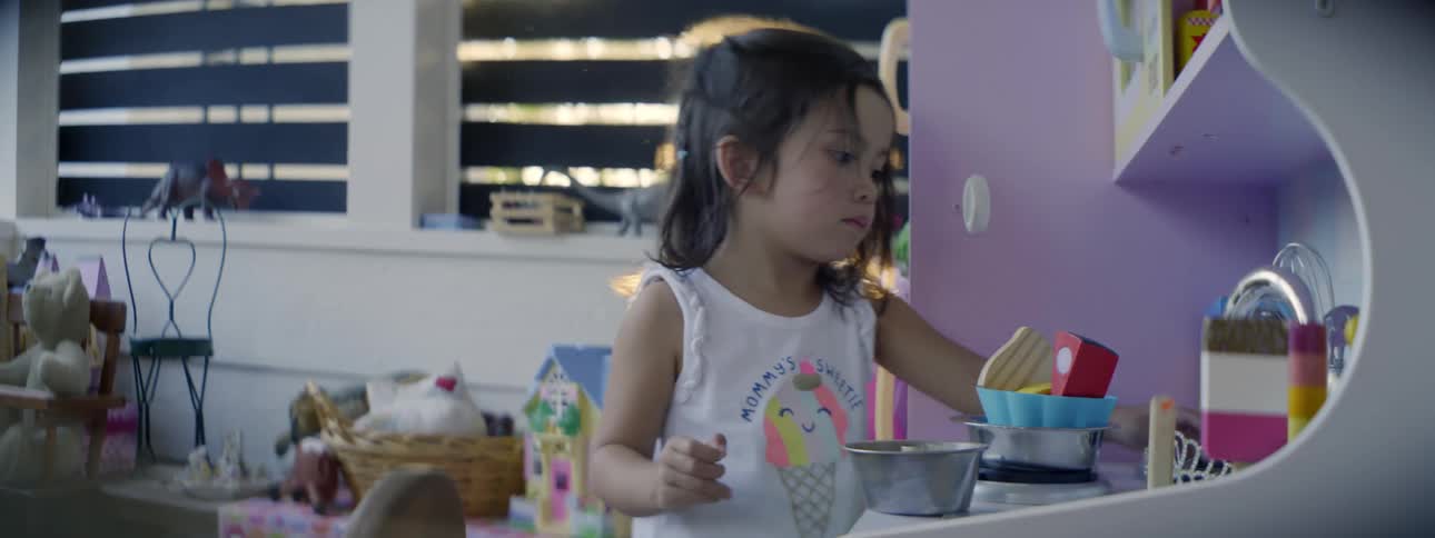 A young girl plays with dishes in a miniature kitchen in a playroom inside