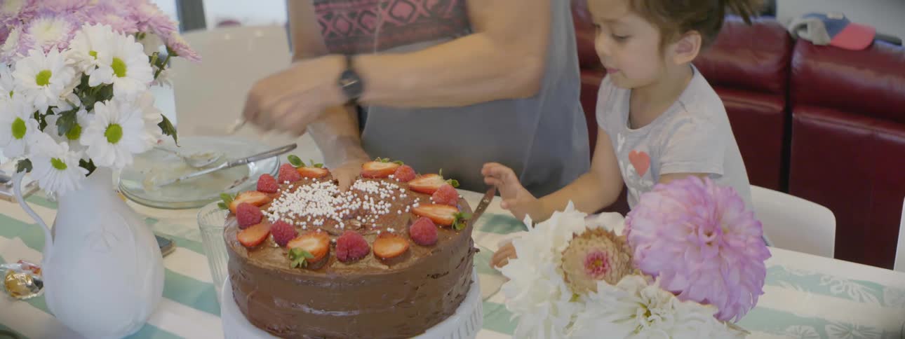 Grandmother cutting a piece of cake at a table while her granddaughter tries to help her