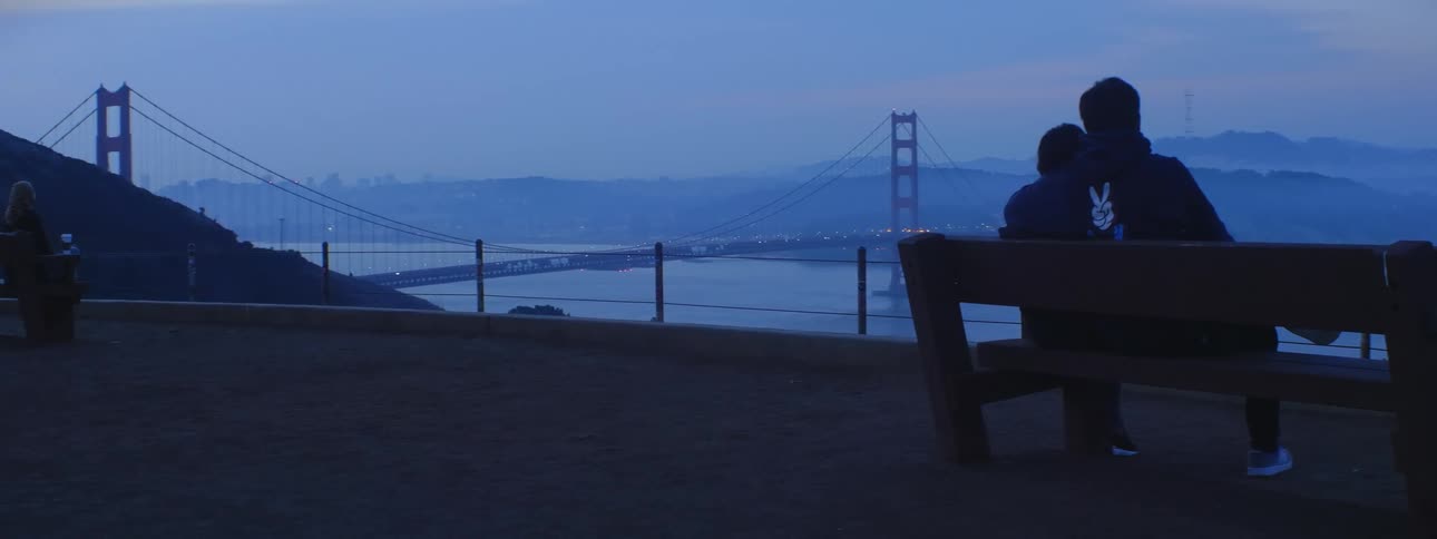 Couple sitting on a bench staring off at the san francisco golden gate bridge