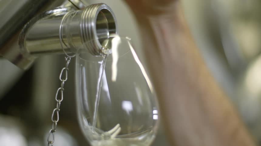 A person uses a faucet to fill a wine glass with wine