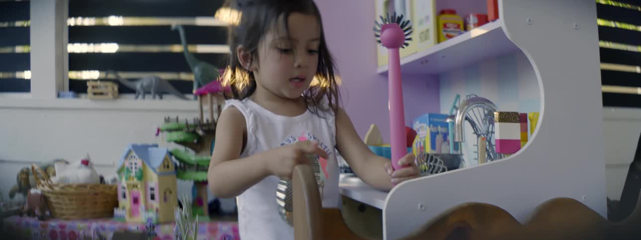 Girl plays with pan in miniature toy kitchen near sink