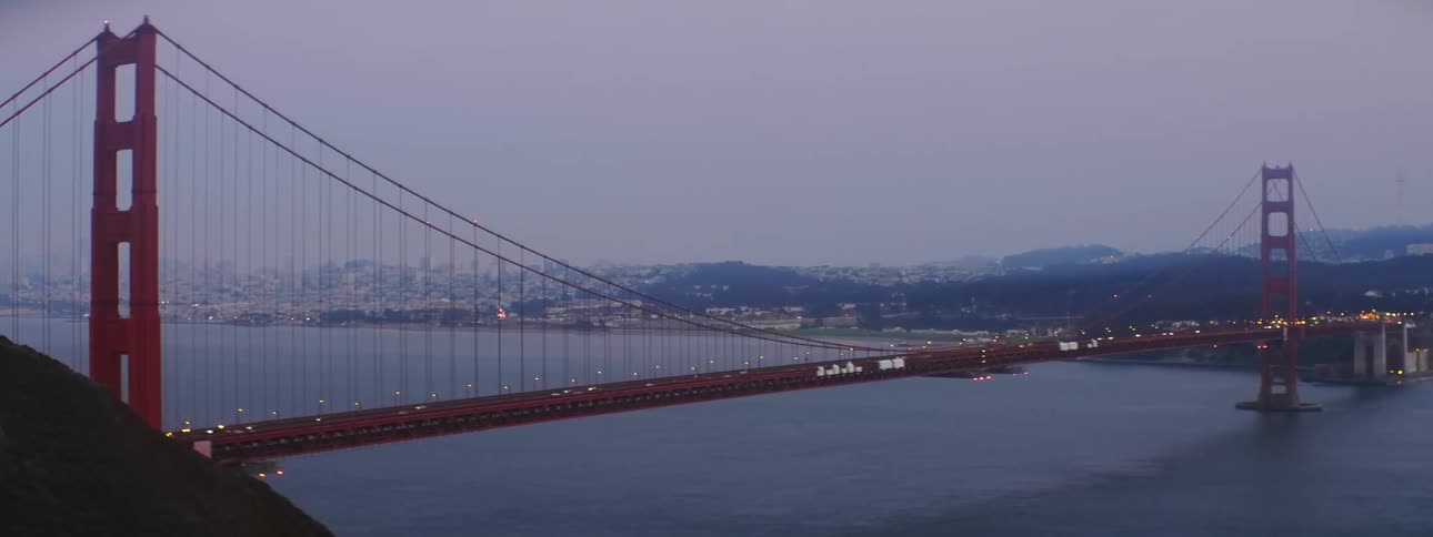 Traffic crosses the golden gate bridge spanning a strait on a foggy evening